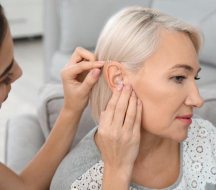 Woman fitting another woman for a hearing aid