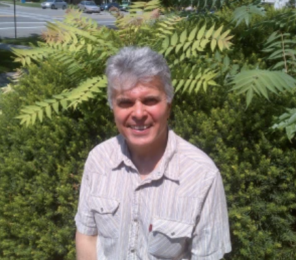 man with gray hair standing in front of a large, green fern outside