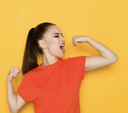 Woman with a brown ponytail flexing her muscles wearing an orange shirt with a yellow background