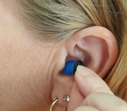 Small blue hearing aid being inserted into a womans ear