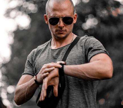 Bald man wearing sunglasses looking down at his watch. 