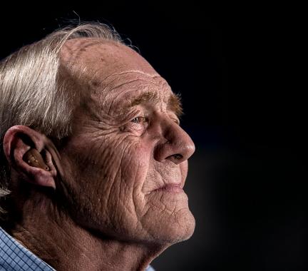 Side profile of elderly man with grey hair wearing a hearing aid.