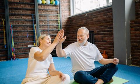 Two older people sitting crosslegged on a mat giving each other a high five