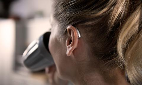 back of a woman's head, she is drinking out of a coffee cup and has a hearing aid on