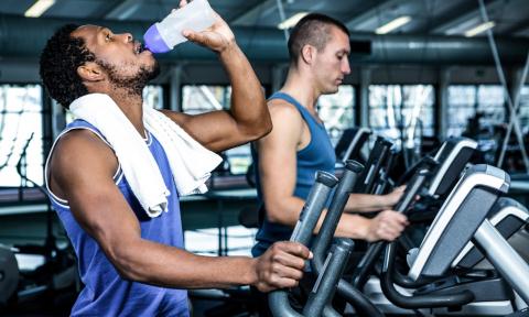 man with beard and dark hair drinking from a water bottle, on a treadmill