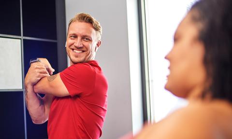 man with a red shirt and blonde hair stretching his arm and smiling