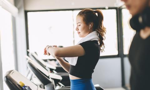 woman with black shirt and blue pants, checking her watch on the treadmill