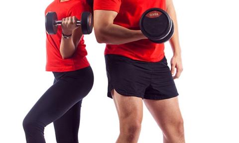 woman and man standing back to back with red shirts, black bottoms and holding a free weight