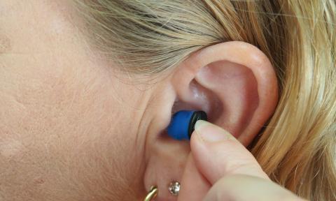 Small blue hearing aid being inserted into a womans ear