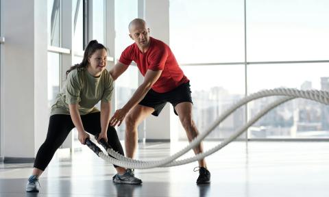 a woman using fitness ropes and a man in a red shirt appears to be coaching her on technique