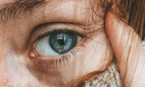 close up picture of a blue eye, with red eyebrow and red hair, cream colored turtleneck sweater