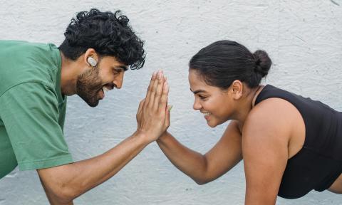 man wearing a green shirt giving a high five to a woman with a black tank top on, both are doing a push up