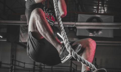 man climbing a rope in a dark gym