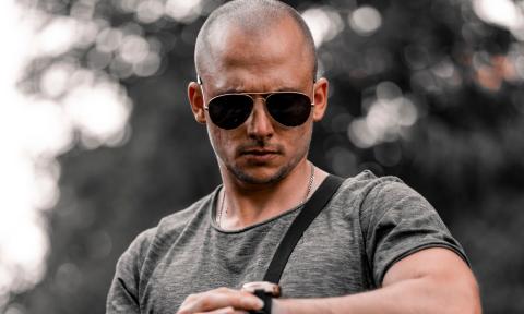 Bald man wearing sunglasses looking down at his watch. 