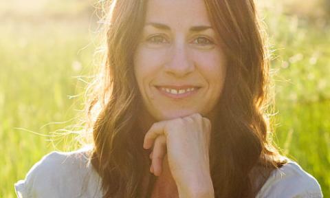 A woman with brown hair smiling and her hand under her chin. 