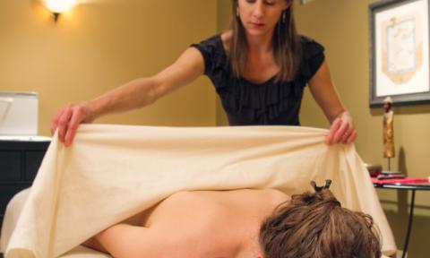 A woman laying on a massage table having her back covered with a sheet. 