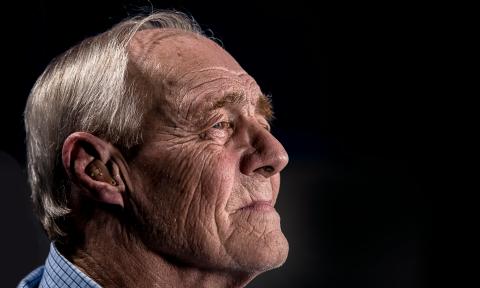 Side profile of elderly man with grey hair wearing a hearing aid.