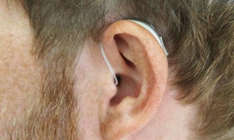 A zoomed in picture of a mans ear wearing a hearing aid. 