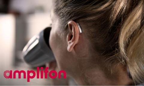 back of a woman's head, she is drinking out of a coffee cup and has a hearing aid on