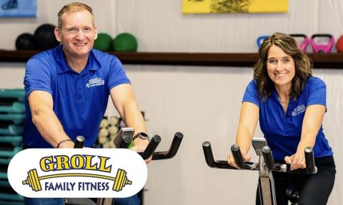 man and woman on stationary bikes looking at the camera and smiling, both are wearing blue shirts, Groll Family Fitness logo bottom left corner