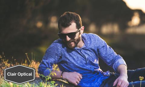 man laying in a field with sunglasses on with Clair Optical logo in bottom left corner