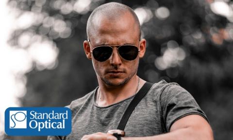 Bald man wearing sunglasses looking down at his watch with Standard Optical logo on bottom left corner