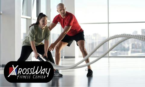 a woman using fitness ropes and a man in a red shirt appears to be coaching her on technique with xrossways fitness center logo on bottom left corner