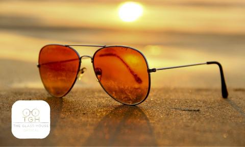 sunglasses on a beach at sunset with the glass house optical logo in the bottom left corner