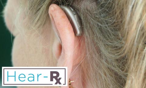 A blonde woman with a hearing aid in her ear with hear-rx logo in bottom left corner