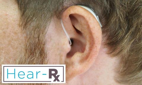 A zoomed in picture of a mans ear wearing a hearing aid with hear-rx logo in the bottom left corner
