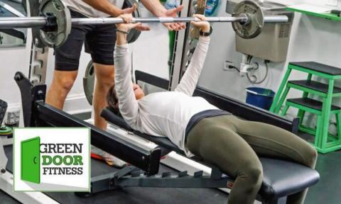 man on weight bench with trainer spotting him, Green Door logo in bottom left corner