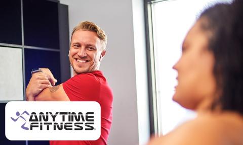 man with a red shirt and blonde hair stretching his arm and smiling, anytime fitness logo in bottom left corner