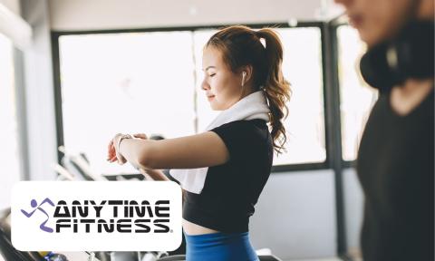 woman with black shirt and blue pants, checking her watch on the treadmill, anytime fitness logo on bottom left corner