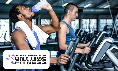 man with beard and dark hair drinking from a water bottle, on a treadmill, Anytime Fitness Logo on the bottom left corner