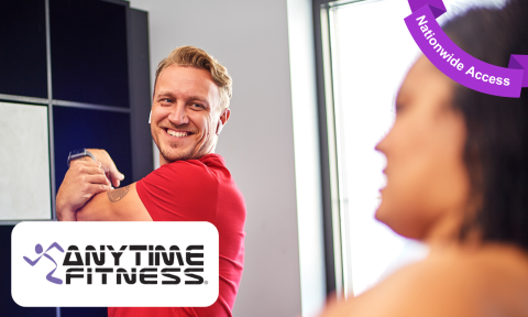 man with a red shirt and blonde hair stretching his arm and smiling, anytime fitness logo in bottom left corner, purple banner reading nationwide access in top right corner