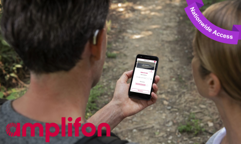 a man and woman on a hiking trail looking at a phone, man is wearing a small, silver hearing aid with amplifon logo in bottom left corner, purple banner top right corner reading nationwide access