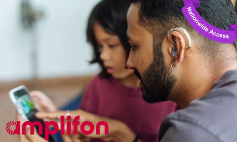 father with hearing aid reading on cell phone screen while daughter sits nearby, with amplifon logo in bottom left corner, purple banner top right corner reading Nationwide access