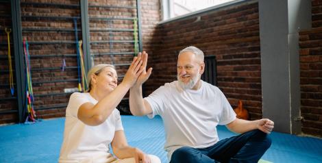 Two older people sitting crosslegged on a mat giving each other a high five