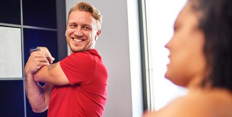 man with a red shirt and blonde hair stretching his arm and smiling