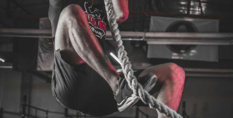 man climbing a rope in a dark gym