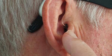 a grey haired man with a small hearing aid in his ear. 