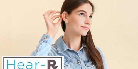 young woman with brown hair and hearing aid cupping her ear, hear-rx logo in bottom left corner