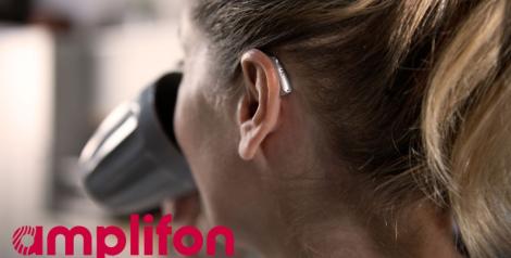 back of a woman's head, she is drinking out of a coffee cup and has a hearing aid on