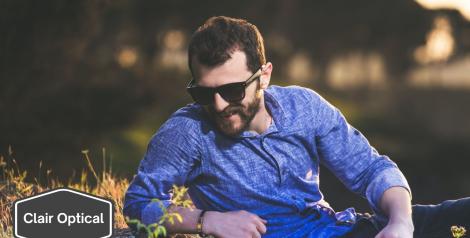 man laying in a field with sunglasses on with Clair Optical logo in bottom left corner