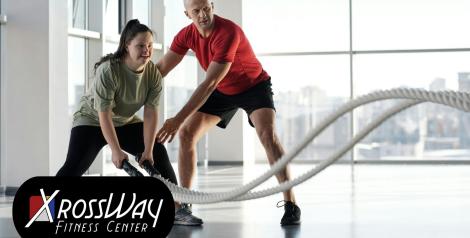 a woman using fitness ropes and a man in a red shirt appears to be coaching her on technique with xrossways fitness center logo on bottom left corner
