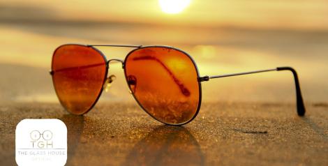 sunglasses on a beach at sunset with the glass house optical logo in the bottom left corner