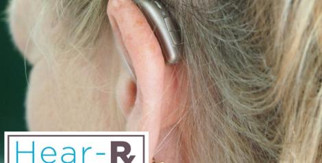 A blonde woman with a hearing aid in her ear with hear-rx logo in bottom left corner