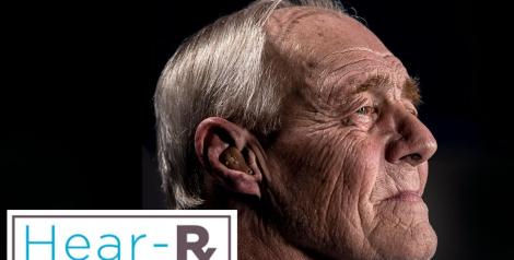 Side profile of elderly man with grey hair wearing a hearing aid with hear-rx logo in bottom left corner