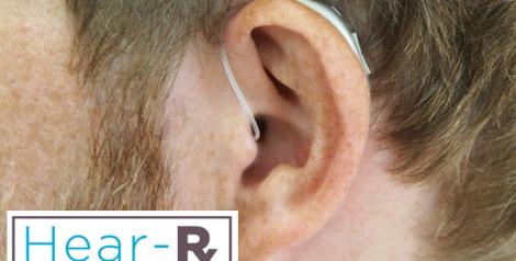 A zoomed in picture of a mans ear wearing a hearing aid with hear-rx logo in the bottom left corner