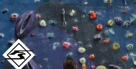 woman looking up at a rock climbing wall, fit stop health logo in bottom left corner